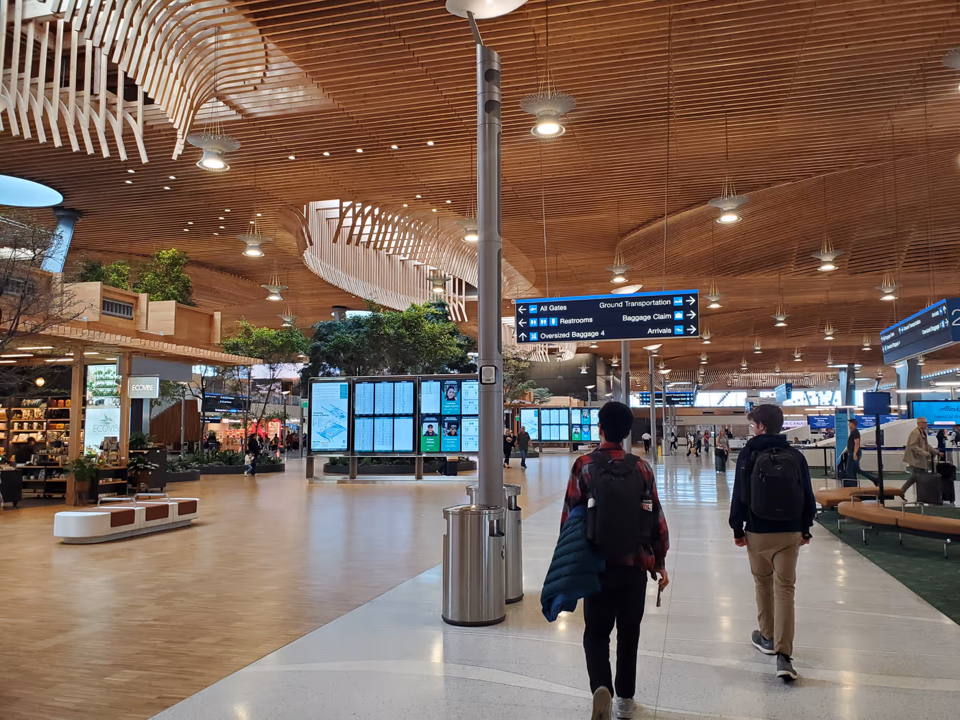 "two students walk through the Portland airport, with its elaborate wooden ceiling clearly visible"