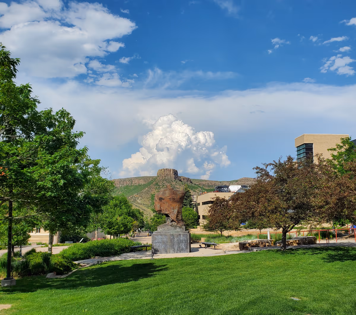 A green field on a college campus. In the background, South Table lies underneath a large cumulonimbus cloud.