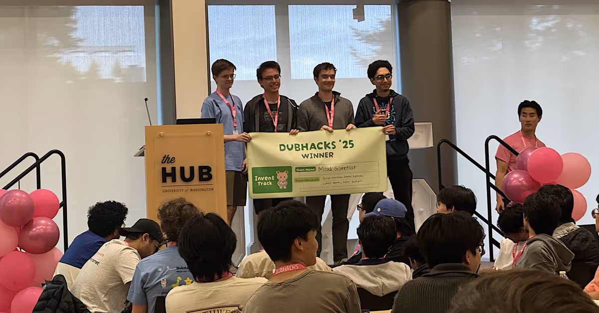 Four students stand on a stage holding a banner that says 'Winner'