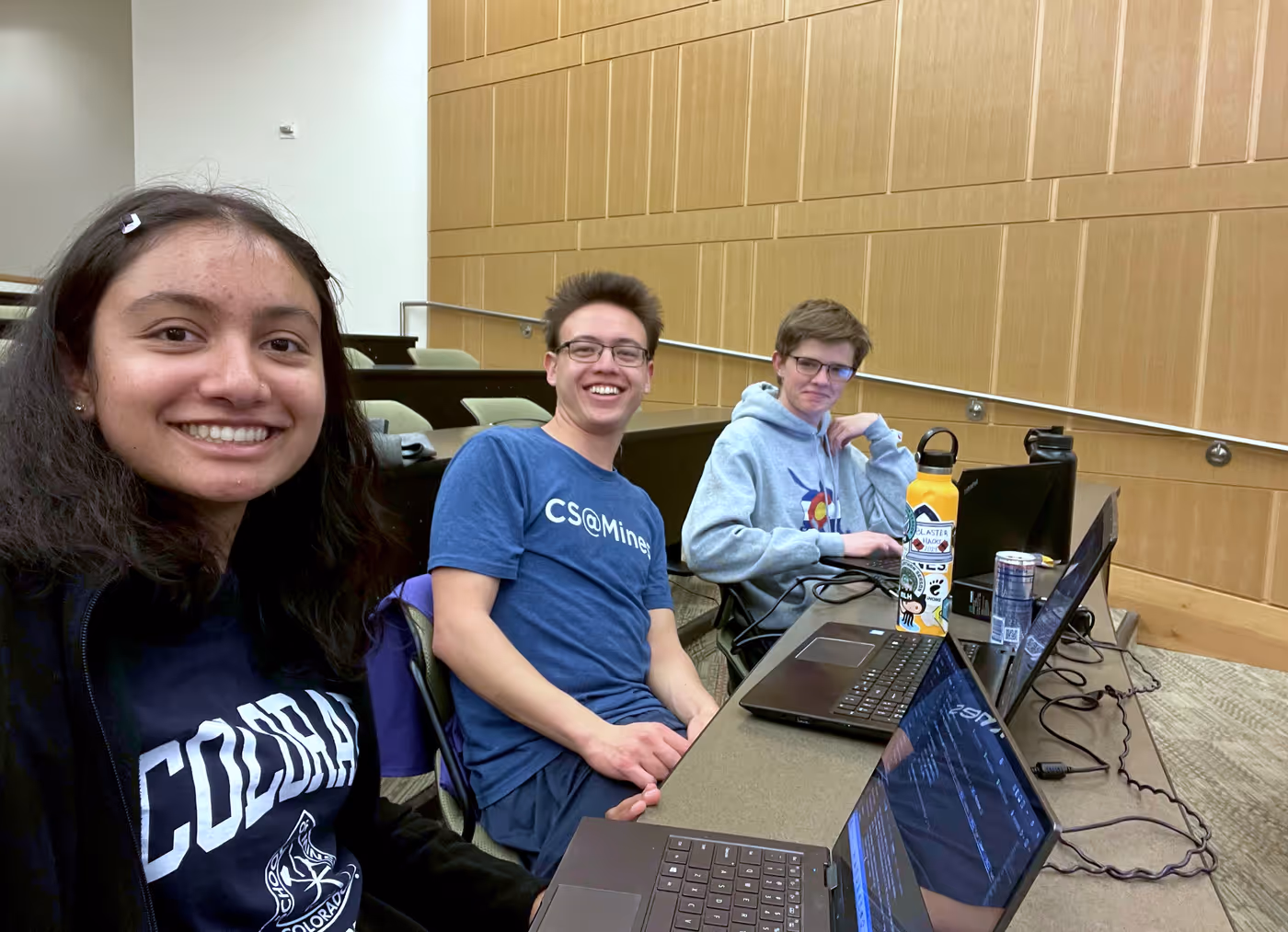 a selfie with three students looking up from their laptops